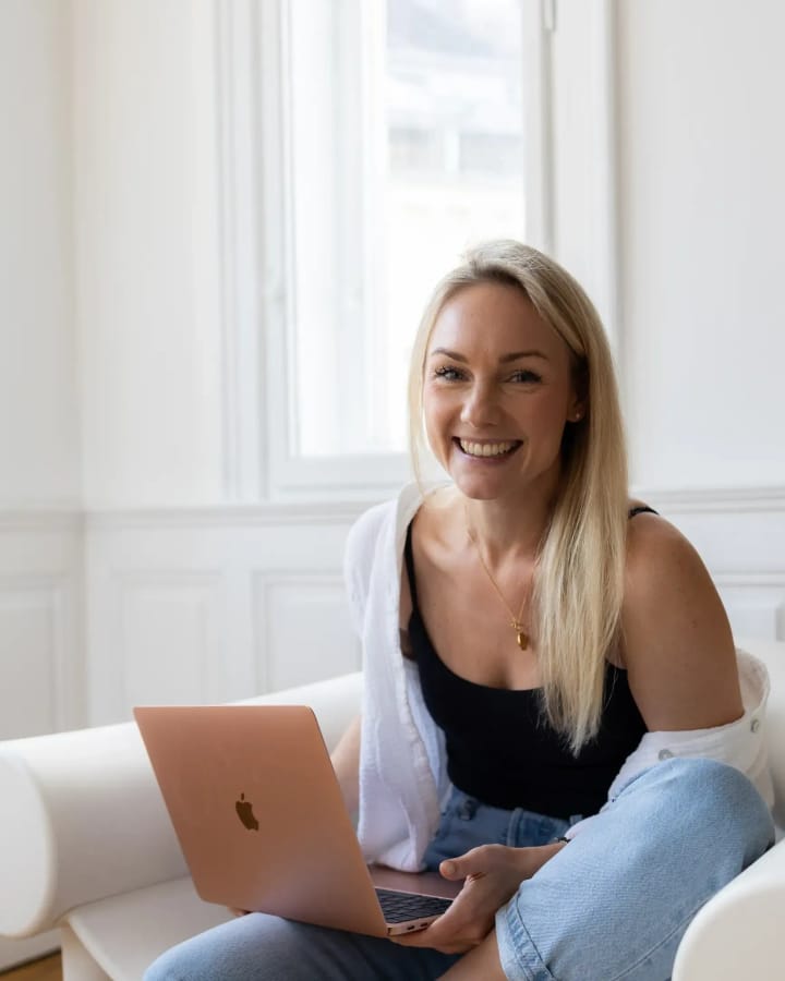 Audrey Hämmerle sitzt lächelnd mit Laptop in einem hellen Altbauzimmer